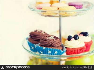 unhealthy eating, sweets, dessert, baking and junk food concept - close up of cake stand with cupcakes and cookies. close up of cake stand with cupcakes and cookies