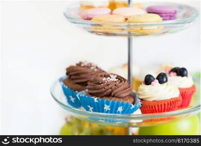 unhealthy eating, sweets, dessert, baking and junk food concept - close up of cake stand with cupcakes and cookies