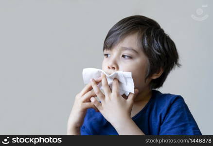 Unhealthy kid with dry skin blowing nose into tissue, Child suffering from running nose or sneezing, A boy catches a cold when season change, childhood wiping nose with tissue