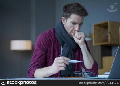 Unhealthy looking young male entrepreneur in warm knitted scarf around his neck coughing looks at digital thermometer in his hand not believing that caught flu while working remotely online from home. Unhealthy looking male entrepreneur in scarf around his neck coughing looks at digital thermometer