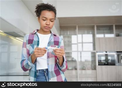 Unhealthy mixed race young girl holding thermometer, checking body temperature at home, has covid fever. Ill sad teen lady patient measuring temp, suffering from flu cold or coronavirus.. Unhealthy mixed race girl holding thermometer, checking body temperature at home, has covid fever