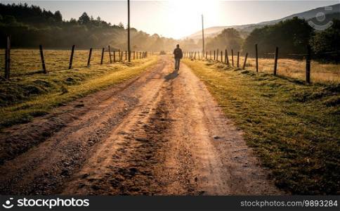 Unidentified man walking along the beautiful a morning country road.
