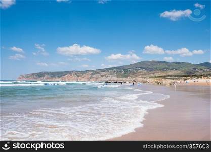Unidentified people with surf board on summer beach and blue ocean water. Summer beach panoramic view