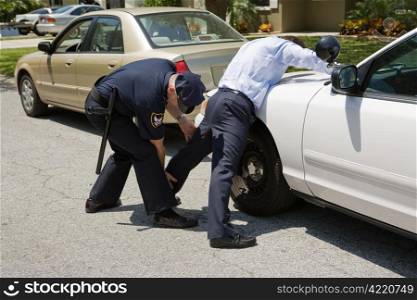 Uniformed police officer patting down a suspect pulled over during a traffic stop.