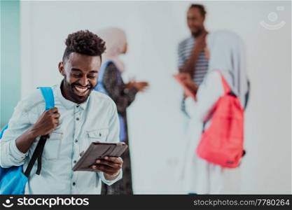 University lifestyle handsome young student man holding a tablet computer and smiling while standing against university with his friends have a team meeting in the background. High-quality photo. High quality photo. University lifestyle handsome young student man holding a tablet computer and smiling while standing against university with his friends have a team meeting in the background. High-quality photo
