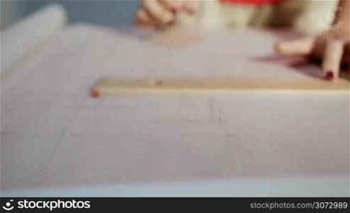 University student of Interior Design doing homeworks, completing housing project for final exam. The girl draws lines on a blueprint with a rule in her studio. Closeup, dolly shot