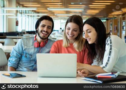 University students sitting together at table using laptop. Group study in university library. Education concept
