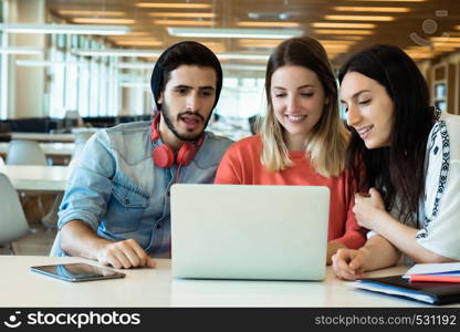 University students sitting together at table using laptop. Group study in university library. Education concept