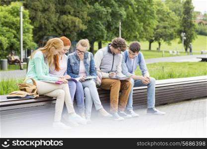 University students studying while sitting on low wall in park