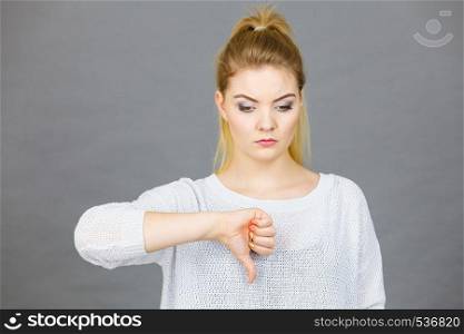 Unlike, dislike, failure gestures concept. Sad woman showing thumb down gesture, studio shot grey background.. Sad woman showing thumb down gesture