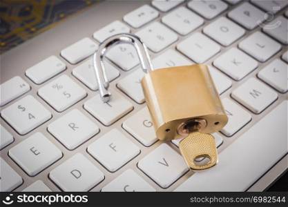 Unlock gold metal padlock with key on modern white keyboard, circuit board on top. Digital data, encryption, online password, cyber security, information privacy, business solution concepts.