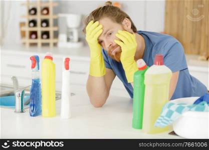 unmotivated man surrounded by household cleaning products