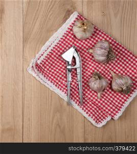 unpeeled fresh garlic fruits and an iron press on a wooden background