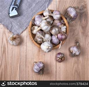 unpeeled fresh garlic fruits in wooden bowl and an iron press , top view