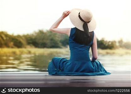 Unplugged Life and Relaxation Concept. Portrait of Young Woman Relaxing by Riverside. Sitting on Wooden Deck and Looking away