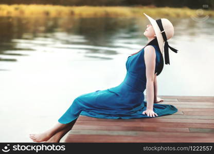 Unplugged Life and Relaxation Concept. Portrait of Young Woman Relaxing by Riverside. Sitting on Wooden Deck and Looking away