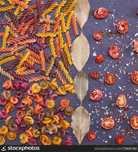 unprepared multi-colored pasta spiral made from wheat flour and cut into halves of cherry tomatoes with salt and spice, full frame