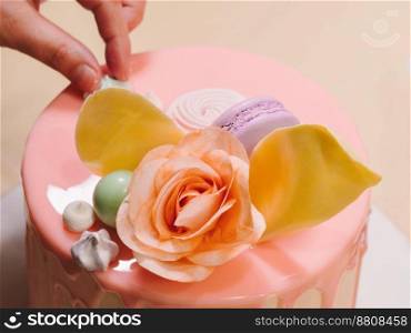 Unrecognisable woman decorating mousse glaze cake, hands detail, focus on the cake. DIY, sequence, step by step, part of series.. Unrecognisable woman decorating mousse glaze cake with rose, macarons, hands detail, focus on the cake. DIY, sequence, step by step, part of series.