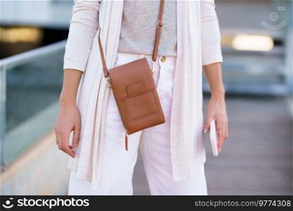 Unrecognisable woman standing near an office building carrying a handbag and a smartphone. Caucasian female in urban background.. Unrecognisable woman standing near an office building carrying a handbag and a smartphone.