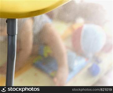 Unrecognizable blurred child playing behind the protective net of a children's playpen. Childhood and toddler