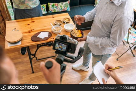 Unrecognizable camera operator recording a streaming cooking tutorial. Selective focus on breakfast bowl in background. Unrecognizable camera operator recording a streaming cooking tutorial.