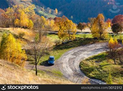 Unrecognizable car on dirty secondary road to mountain pass in autumn Carpathian mountains and multicolored yellow-orange-red-brown trees on slopes (Rakhiv pass, Transcarpathia, Ukraine).