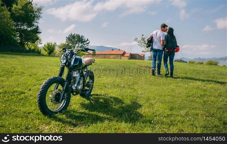 Unrecognizable couple kissing while walking on the field with parked motorbike. Couple kissing and walking on the field with motorbike