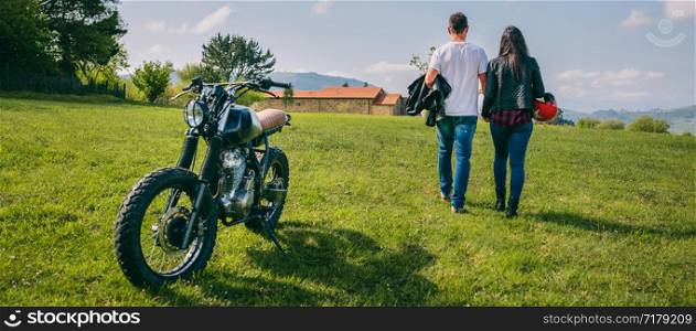 Unrecognizable couple walking on the field holding hands and parked motorbike. Couple walking on the field holding hands and motorbike