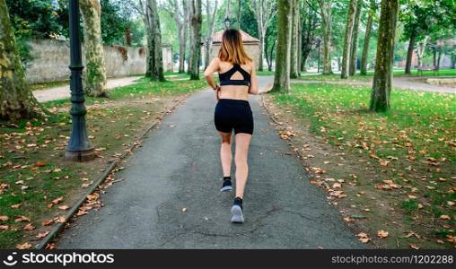 Unrecognizable female athlete running through a park. Female athlete running through a park