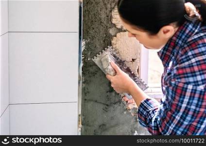 Unrecognizable female bricklayer leveling cement with a trowel to tile the wall. Female bricklayer leveling cement with a trowel