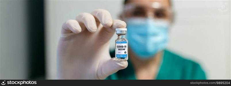 Unrecognizable female laboratory technician showing vial of coronavirus vaccine. Selective focus on vial in foreground