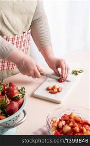 Unrecognizable housewife cutting in small pieces the strawberries. The process of making strawberry jam at home with organic fruits. Woman preparing the fruits for jam