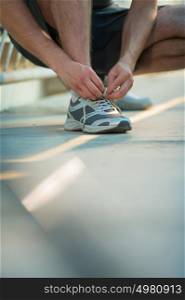 Unrecognizable man lacing his shoes before running outdoors