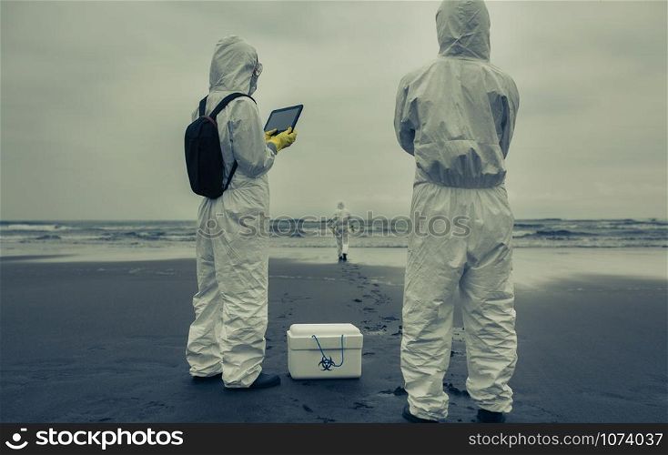 Unrecognizable people with bacteriological protection suits looking for evidence at sea. People with bacteriological protection suits looking for evidence at sea