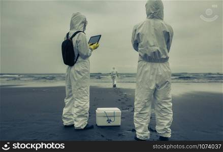 Unrecognizable people with bacteriological protection suits looking for evidence at sea. People with bacteriological protection suits looking for evidence at sea