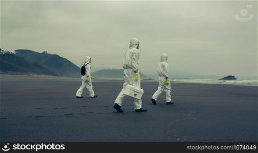 Unrecognizable people with bacteriological protection suits walking on the sand of the beach. People with bacteriological protection suits walking on the beach