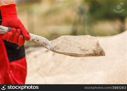 Unrecognizable person worker using shovel standing on industrial construction site, working hard on house renovation.. Person using shovel on construction site