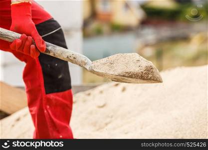 Unrecognizable person worker using shovel standing on industrial construction site, working hard on house renovation.. Person using shovel on construction site