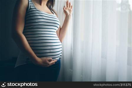 Unrecognizable pregnant holding her belly in front of a curtain. Unrecognizable pregnant holding her belly