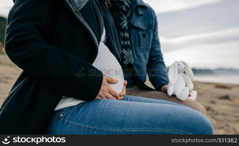 Unrecognizable pregnant on the beach with her partner with a stuffed toy. Pregnant on the beach with her partner