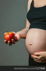 Unrecognizable pregnant woman holding a red apple