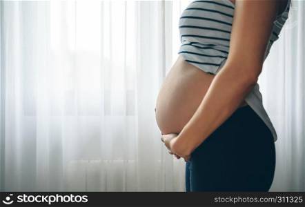 Unrecognizable pregnant woman holding her tummy in the bedroom. Pregnant woman holding her tummy