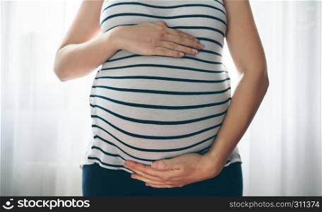 Unrecognizable pregnant woman holding her tummy in the bedroom. Pregnant woman holding her tummy