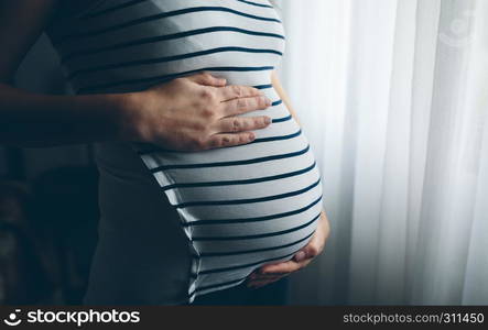 Unrecognizable pregnant woman holding her tummy in the bedroom. Pregnant woman holding her tummy