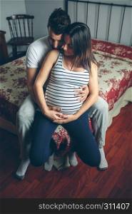 Unrecognizable pregnant woman touching her belly embraced by her husband. Pregnant woman embraced by her husband