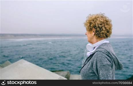 Unrecognizable senior sportswoman with headphones looking at the sea. Senior sportswoman looking at the sea