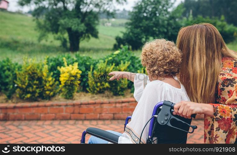 Unrecognizable senior woman in a wheelchair with her daughter looking at the landscape. Senior woman in a wheelchair with her daughter