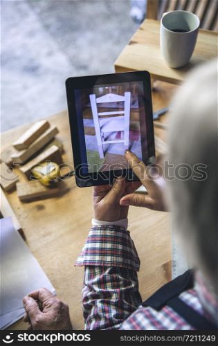 Unrecognizable senior woman working in a carpentry workshop looking tablet with chair design. Unrecognizable senior woman in a carpentry looking tablet