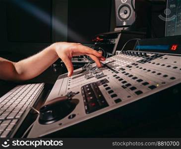 Unrecognizable sound producer or engineer rotates scrolls wheel on mixing console in professional recording studio. Musician working on new song. Hands close up. High quality photo. Unrecognizable sound producer or engineer rotates scrolls wheel on mixing console in professional recording studio. Musician working on new song. Hands close up.