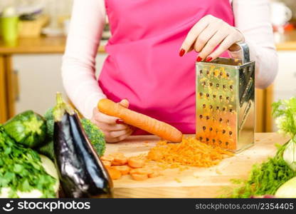 Unrecognizable woman grating carrot on metal grater, kitchen utensil making food preparing healthy vegetable salad.. Woman grating carrot on metal grater